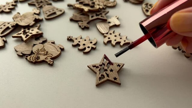 Coating wooden blank in shape of Christmas star using red nail polish. DIY xmas ornaments at home. prepare to decorate Christmas tree POV. Film grain texture. Soft focus. Live camera. Blur. Candid
