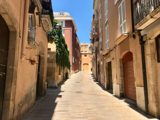 Fototapeta na wymiar Tarragona, Spain, June 2019 - A narrow city street with buildings on the side of a building