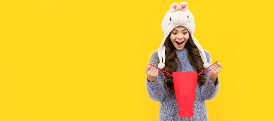 happy child in sweater and hat hold shopping bag on yellow background, xmas shopping. Banner of shopping child girl, studio poster header with copy space.