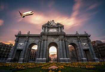 Obraz premium Alcala Gate of Madrid with sunset clouds on sky and an airplane