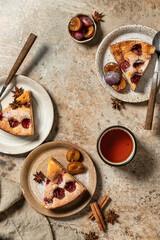 Pieces of The New York Times Plum Cake pie with tea on brown textured background, top view
