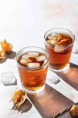 Orange healthy cold beverage cocktails decorated with physalis berry on marble background with text space. Drink Photo with hard light and clear shadows. Autumn party concept