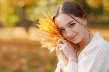 girl in yellow clothes in autumn park rejoices in autumn holding yellow leaves in her hands, warm autumn concept