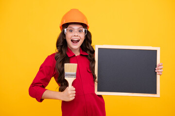 Excited teenager girl painter in helmet with painting brush. Blackboard for copy space. Child in hard hat. Kid builder painter on construction site. Renovation and repair.