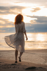 curly girl at sunset runs on the beach. flying dress