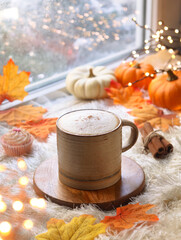 A cup of healthy pumpkin spices latte with mousse of milk topped with ground spices. Cinnamon sticks and fall leaves with small squash in background. With light bokeh and cozy ambiance of autumn  