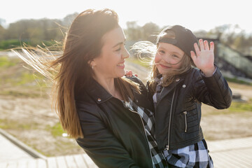 Close up portrait of happy little adorable girl smiling, having fun and waiving ay camera while spending time with her mother outdoor in sunlight 