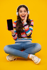 Teenager girl use smart phone, share social media, chatting by mobile phone wear stylish casual trendy clothes isolated over yellow background. Kid showing blank screen mobile phone, mockup copyspace.