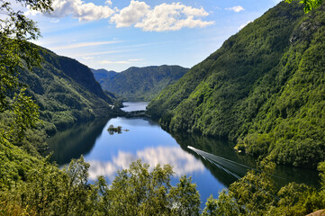 Fjord in Norway with forested mountains, deep valley and water with ship and island.
