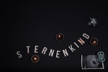 Buchstaben mit dem Wort Sternenkind mit Kerze und Schnuller auf schwarzen Hintergrund mit Platz für Text
