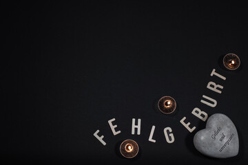 Buchstaben mit dem Wort Fehlgeburt mit Kerze, Ultraschallbild und Schnuller auf schwarzen Hintergrund mit Platz für Text