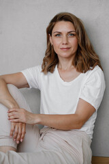 Closeup portrait of happy creative young woman smiling and looking directly to the camera over grey wall. Female at her 40s relaxed in white t-shirt