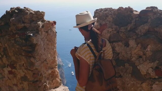 A woman tourist with a backpack and a hat sits on the fortress wall in the fortress of Alanya, Turkey. Beautiful sea landscape with a fortress.