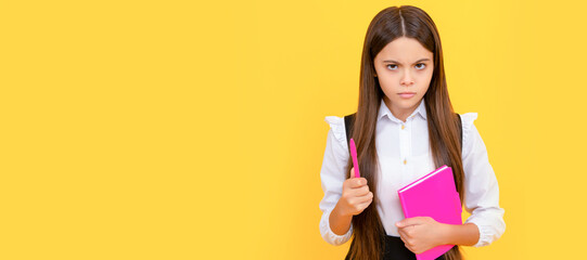 Serious frown child hold school book and pen yellow background. Portrait of schoolgirl student, studio banner header. School child face, copyspace.