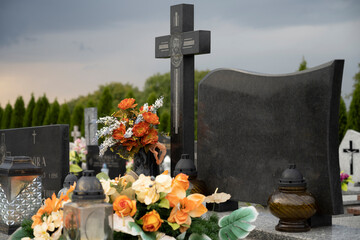 Grave with cross and empty board and cemetery in the background.