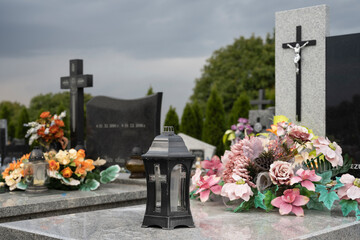 Beautiful artificial bouquet and candle on the grave at all saints day with cross in the background.