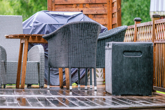 Heavy rain at wooden terrace with summer chairs, wooden table, grill covered against of rain. Blurry green forest at background. Everything is very wet. Countryside, day time. close up photo
