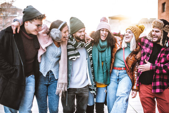 Group of happy millennial friends walking in the city at Christmas time - Young tourists laughing and joking in winter clothes - Concept of friendship, fun and youthful lifestyle