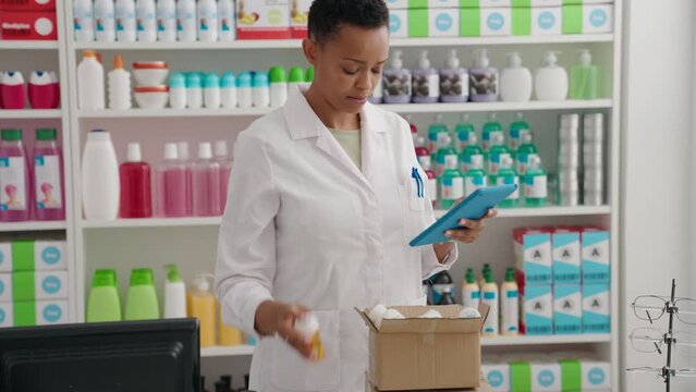 African american woman pharmacist using touchpad holding packages at pharmacy