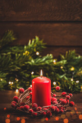 Merry Christmas and Happy New Year! Red candle, a wreath of red berries and fir branches on a wooden background