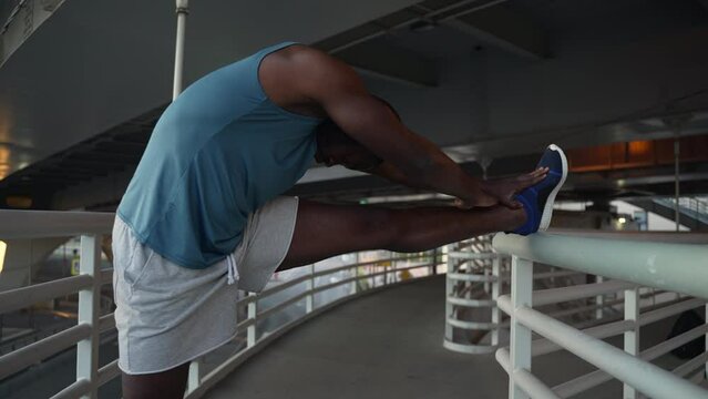 4k Young male athlete is warming up body and training on bridge in city outdoors spbas. Close view of american african guy stretches legs and trains hard, gets ready for fight and poses for camera