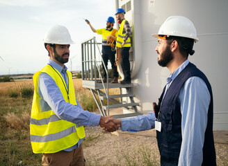 Two male engineers shake hands in a field of windmills. Agreement, renewable energy, energy...