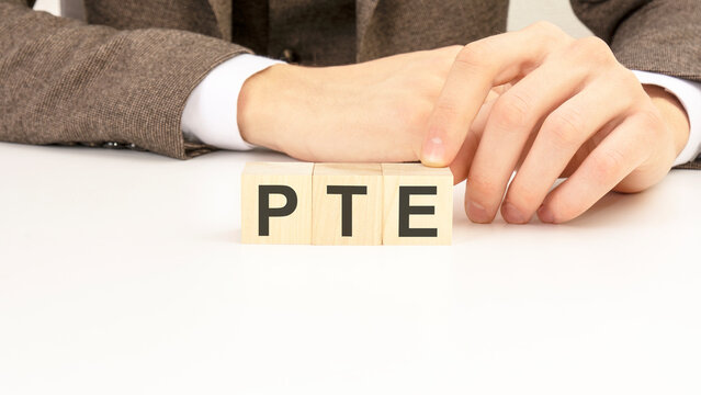 hand holding wooden cube blocks with text pte - Pearson Tests of English - on white table background. marketing concepts