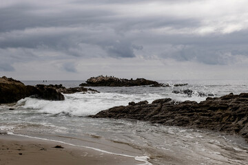 Fototapeta na wymiar Bird Rock and waves crashing on the shore rocks of Laguna Beach, California on a cloudy day.