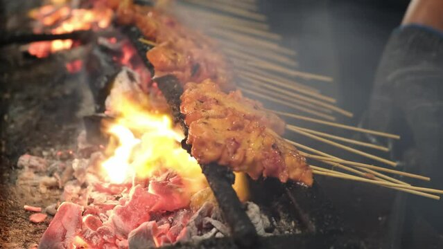 Skewered chicken satay over charcoal fire barbecue with flame and smoke. Famous street food of Malaysia, Singapore, Thailand