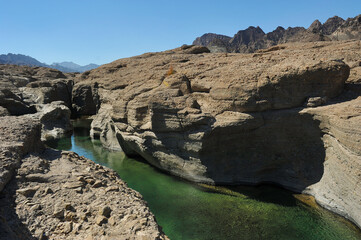 Fresh, clear rock pool in Hatta, an inland exclave of Dubai, United Arab Emirates. Exotic Wadi Al Qahfi on a summer day. Rugged landscape with vibrant green waters. UAE daytrip and travel destination.