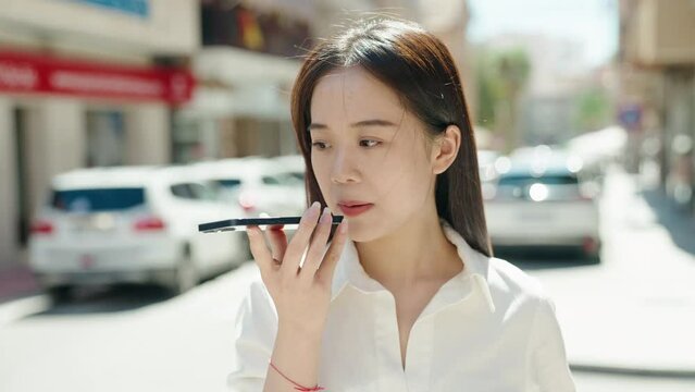 Young chinese woman talking on smartphone with serious expression at street