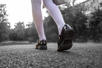 The legs of a child in black shoes walk along the sidewalk.