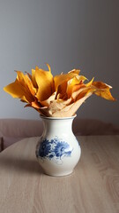Still life of golden yellow leaves in a white porcelain vase with blue floral patterns.