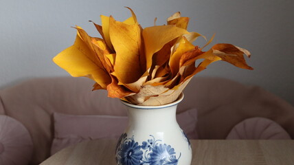 Still life of golden yellow leaves in a white porcelain vase with blue floral patterns.