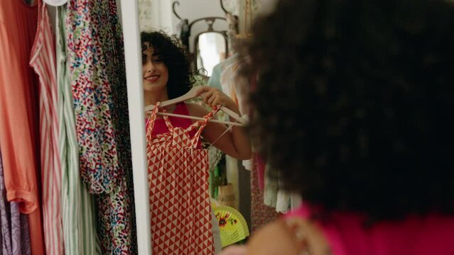 Young middle eastern woman customer looking clothes on mirror at clothing store