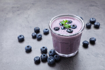 Glass of blueberry smoothie with mint and fresh berries on grey table. Space for text