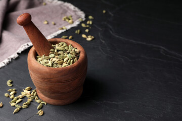 Mortar and pestle with dry cardamom pods on dark grey table, space for text