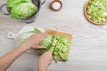 Woman cutting Chinese cabbage at white wooden kitchen table, top view - obrazy, fototapety, plakaty