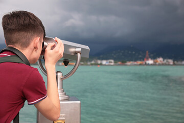 Teenage boy looking through mounted binoculars at mountains. Space for text