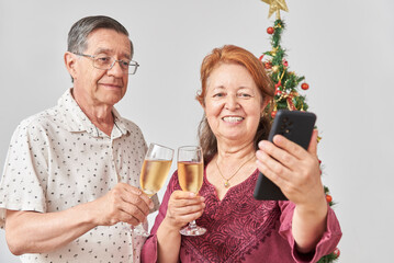 Happy senior hispanic couple talking by video call with a smartphone while toasting during Christmas or New Year, celebrating holidays at home, together.