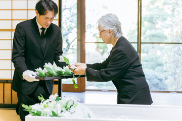 お葬式の納棺式で花入れの儀をする高齢者女性
