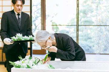 お葬式の納棺式で花入れの儀をする高齢者女性（泣く）
