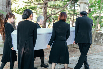 お葬式で棺桶を霊柩車に運ぶ遺族
