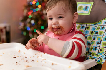 Fototapeta premium cute toddler eating chocolate candy in his high chair