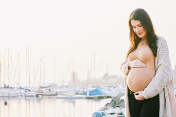 Fototapeta na wymiar Outdoor portrait of beautiful pregnant woman touching belly, early morning walk next to lake