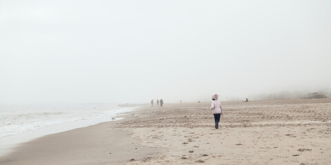 Fototapeta na wymiar young girl is playing on an empty beach during a foggy, cold day