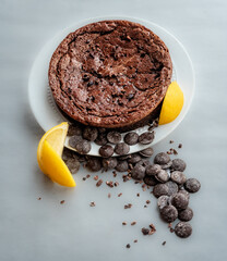 Chocolate-olive oil cake with lemon garnish on a white plate with chocolate morsel and lemon quarters garnish