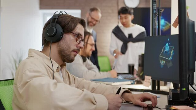 Caucasian male artist designer in glasses draws on a tablet a 3D model of a magic book for a computer game in the office of a project development studio. 