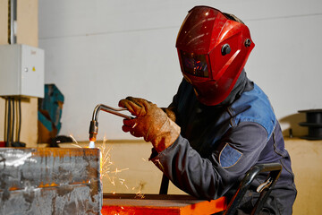 Welder in mask cuts steel beam with cutting blowpipe in shop