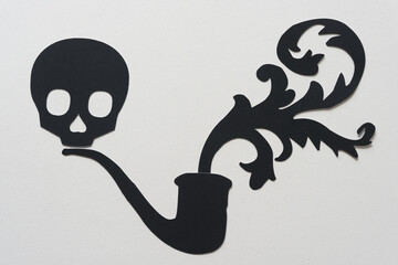 black paper skull head, pipe, and decorative floral shape on blank paper